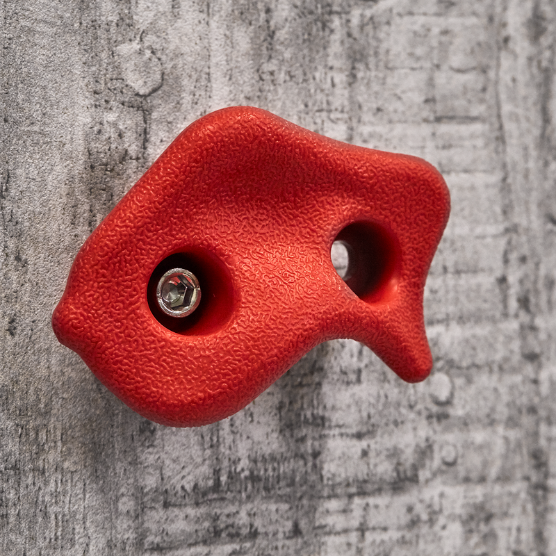  En rød plast klatresten fra Nordic Play der er skruet ind i en væg 